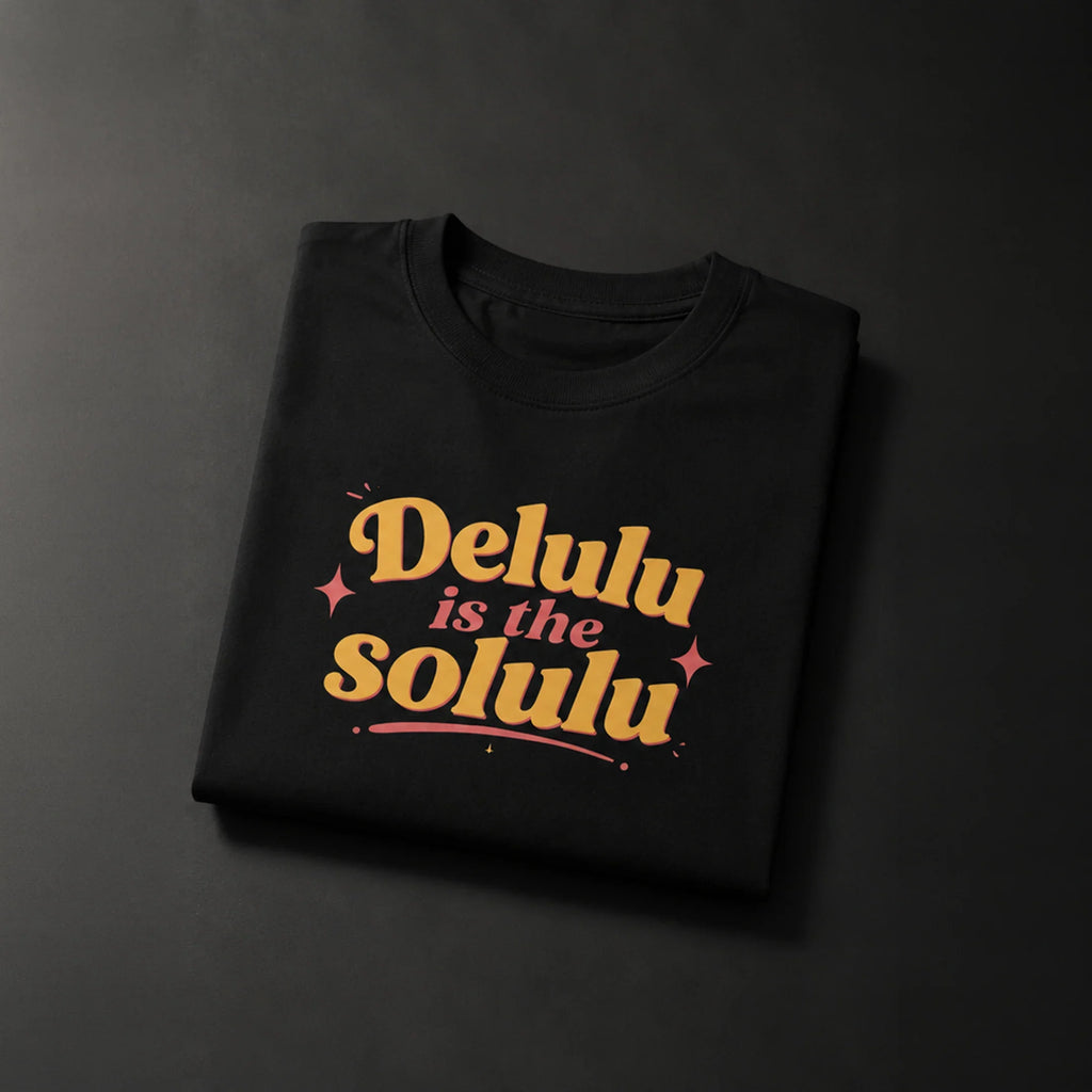Black folded t-shirt with 'Delulu is the Solulu' in bold yellow and pink retro font, perfect for streetwear lovers.
